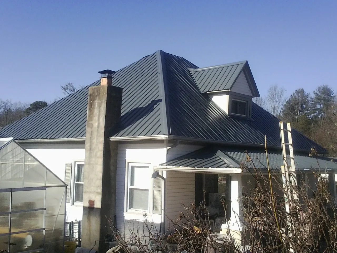 Dark blue standing seam metal roof on a white farmhouse with dormer — Slate & Tile Roof Repair by Roofing Brothers in Grandview