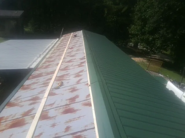 Old rusted panels beside newly installed green metal roofing — Wind Damage Roof Repair by Roofing Brothers in Grandview